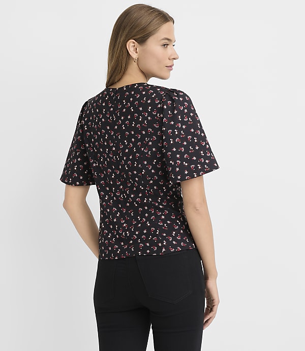 A woman in a floral print top and black pants stands against a plain white background.