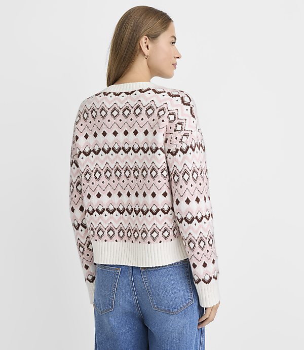 A woman in a patterned sweater and jeans stands against a plain white background.