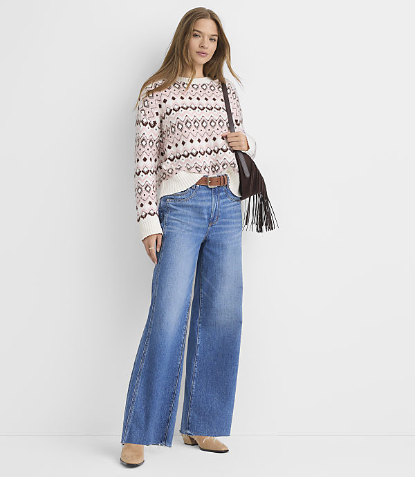 A woman in a patterned sweater and wide-leg jeans stands against a plain white background.