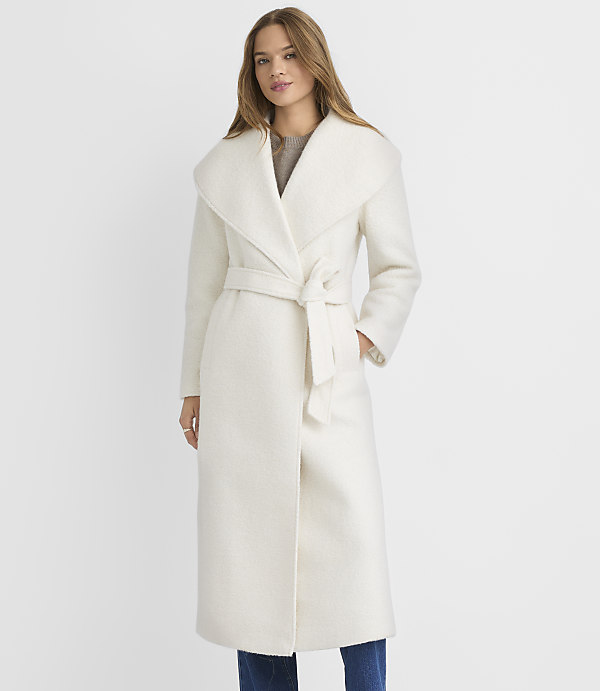 A woman in a cream-colored coat stands against a plain white background.
