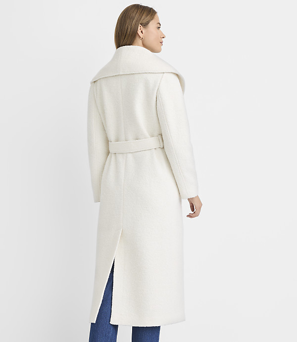 A woman in a cream-colored coat stands against a plain white background.