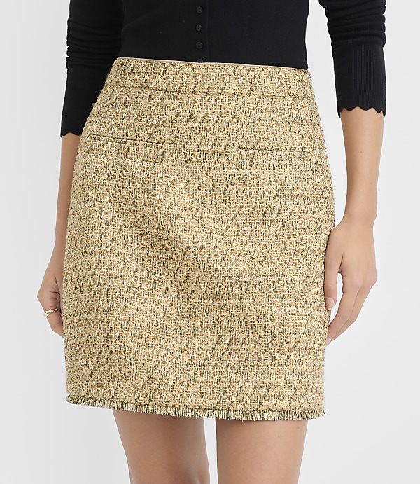 A woman models a textured tweed mini skirt with frayed hem in the foreground, against a plain white background.