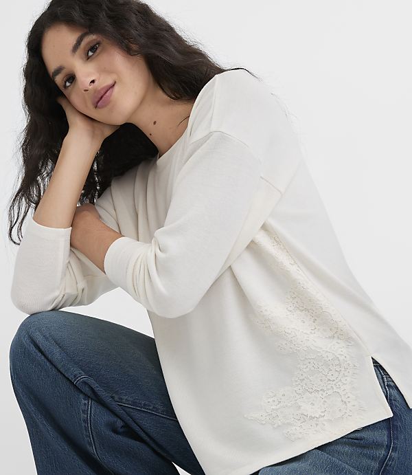 A woman in a cream-colored top and blue jeans poses against a plain white background.