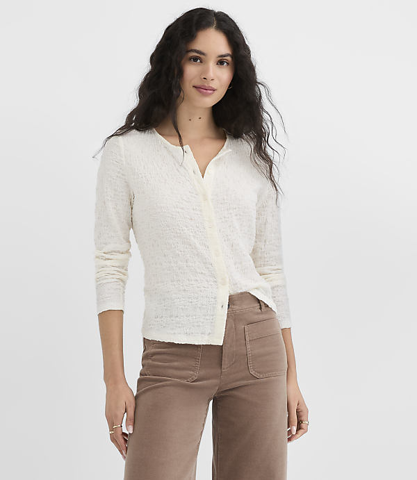 A woman in a cream-colored cardigan and brown corduroy pants stands against a plain white background.
