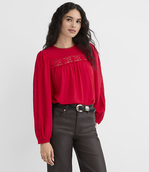 A woman in a red lace-trimmed blouse and dark pants stands against a plain red background.