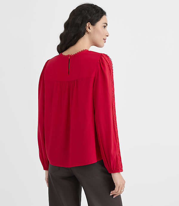 A woman in a red blouse stands against a plain gray background.