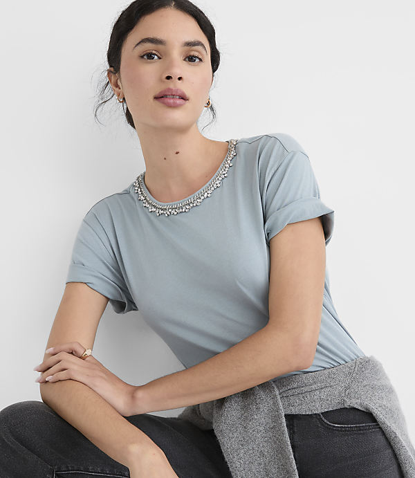 A woman in a light blue t-shirt with a jeweled neckline poses against a plain white background.