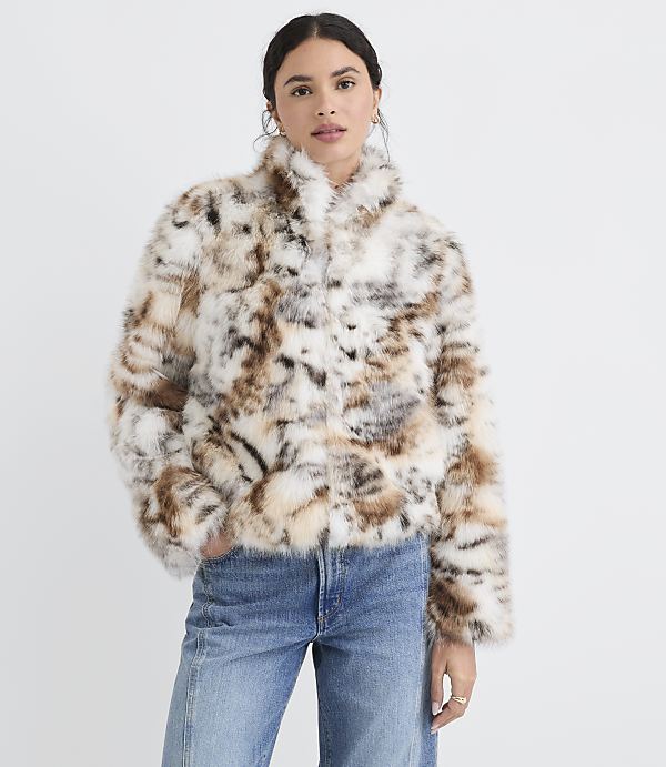 A woman in a patterned faux fur jacket and jeans stands against a plain white background.