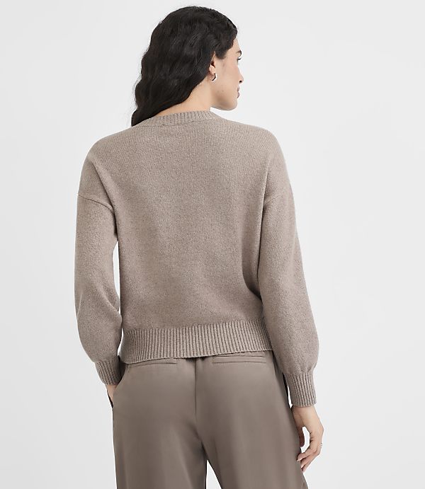A woman in a taupe sweater and pants stands against a plain white background.