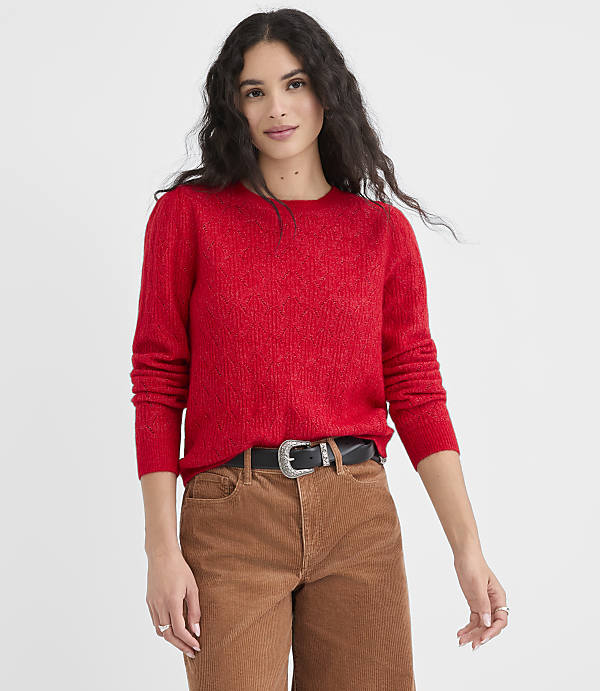 A woman in a red sweater and brown pants stands against a plain white background.