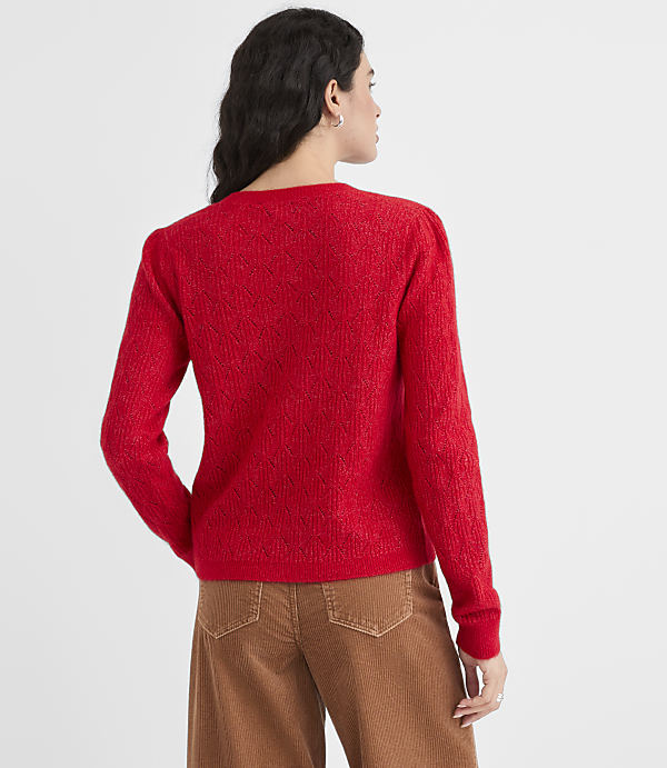 A woman in a red sweater and brown pants stands against a plain white background.