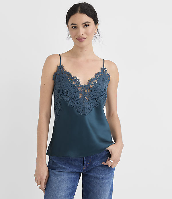 A woman in a teal lace-trimmed camisole and blue jeans stands against a plain white background.