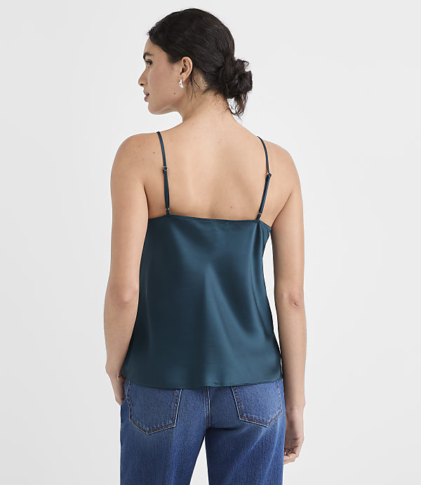 A woman in a teal camisole and blue jeans stands against a plain white background.