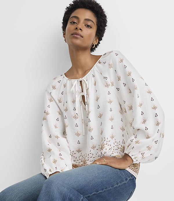 A woman in a patterned blouse and jeans poses against a plain white background.