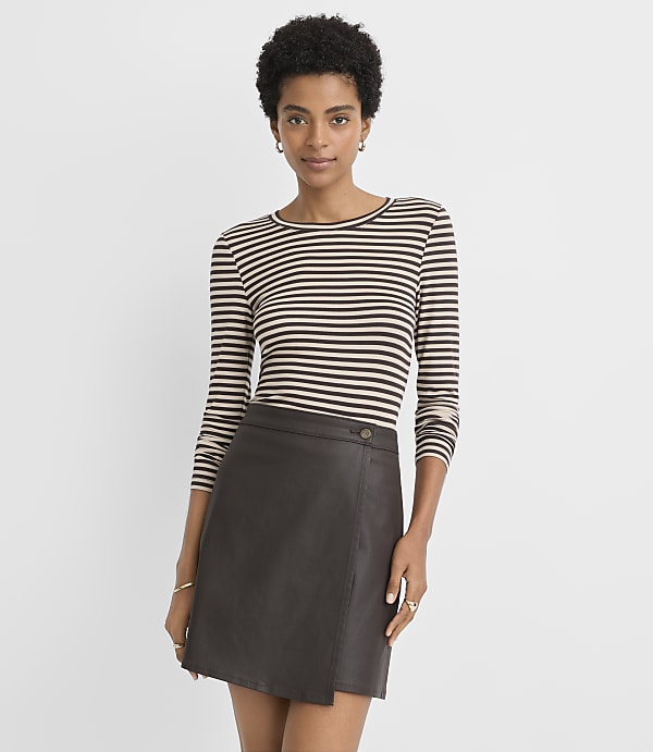 A woman in a striped shirt and a brown leather skirt stands against a plain, light gray background.