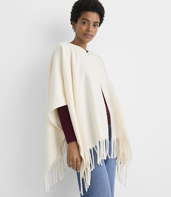 A woman in a cream-colored fringed poncho stands against a plain white background.