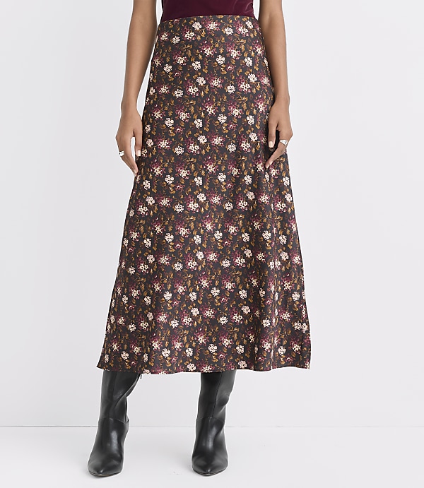 A woman in a floral midi skirt and black boots stands against a plain white background.