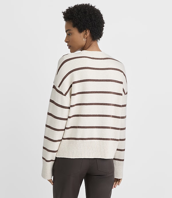A woman in a cream and brown striped sweater stands against a plain white background.