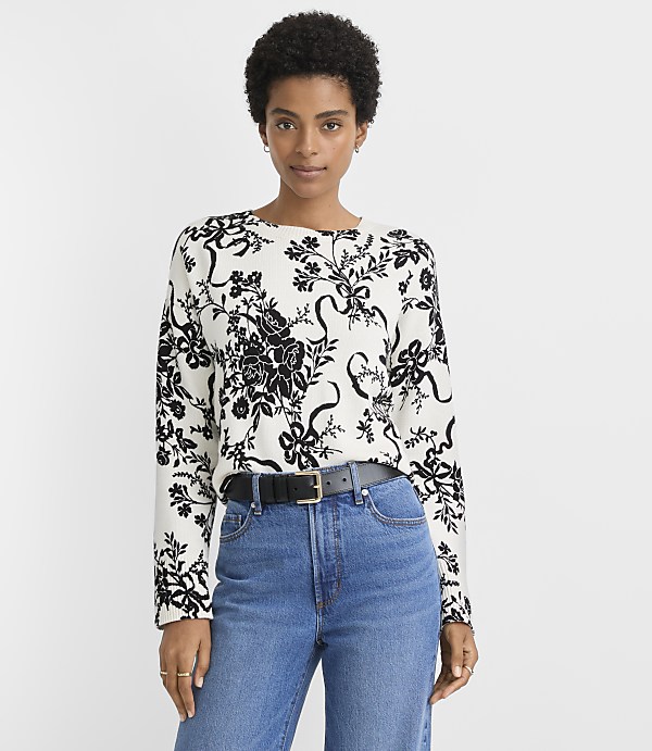 A woman in a floral sweater and jeans stands against a plain white background.