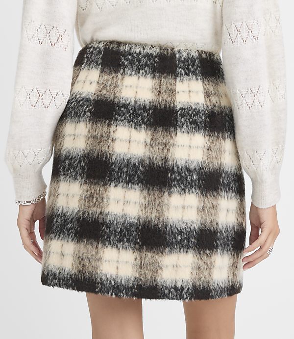 A woman wears a plaid mini skirt and a cream sweater with eyelet details on the sleeves.