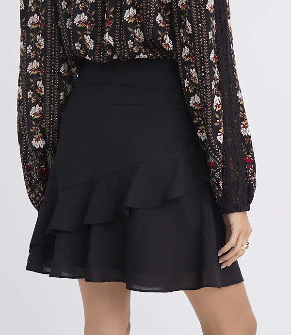 A woman in a black ruffled skirt and a floral print blouse stands against a plain white background.
