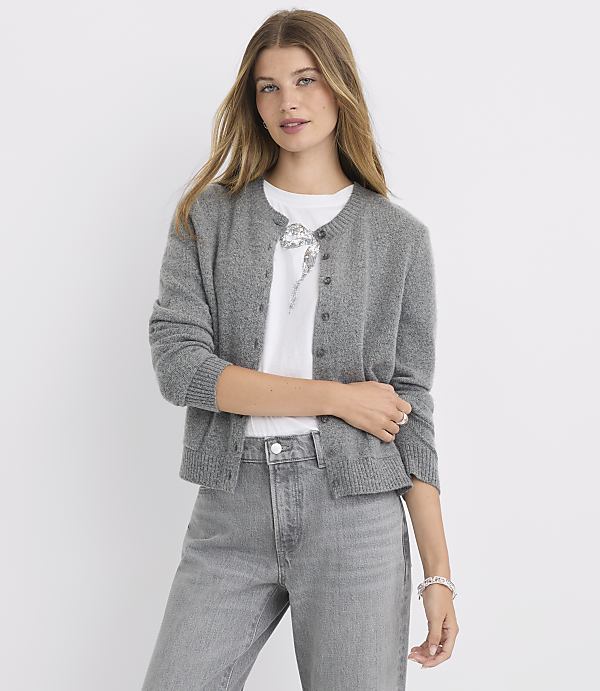 A woman in a gray cardigan and jeans stands against a plain white background.