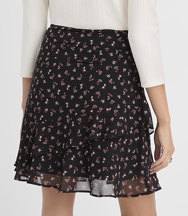 A black floral print mini skirt with ruffled tiers is worn by a person against a plain gray background.