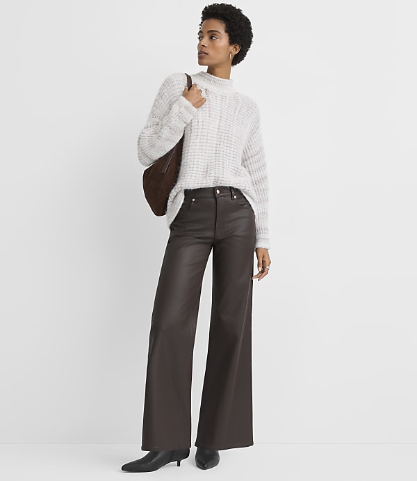 A woman in a cream sweater and brown wide-leg pants stands against a plain white background.