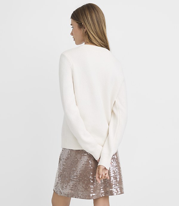 A woman in a cream sweater and sequined skirt stands against a plain white background.