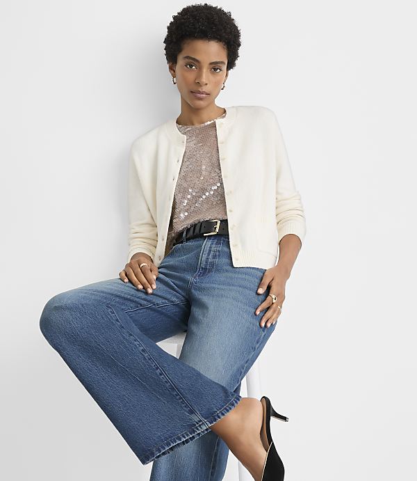A woman in a teal cardigan and blue jeans stands against a plain white background.