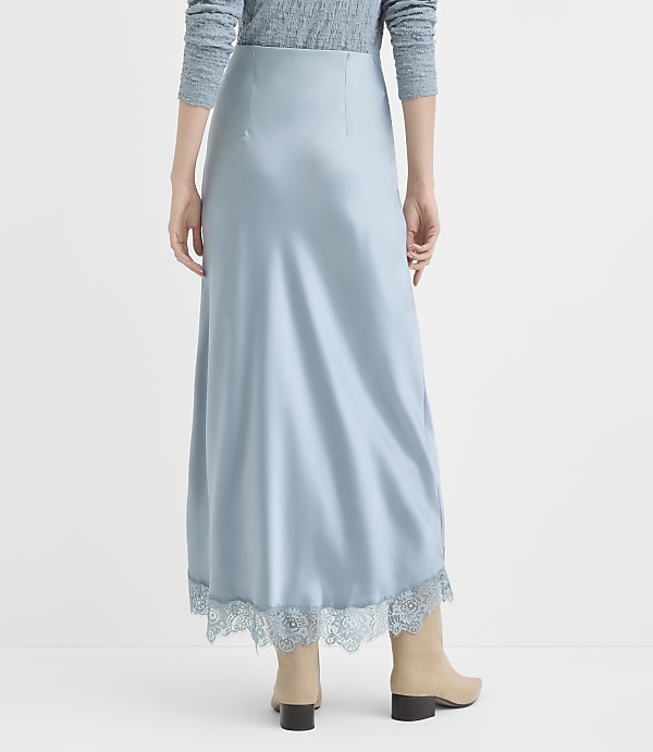 A person wearing a light blue satin skirt with lace trim stands against a plain, light gray background.