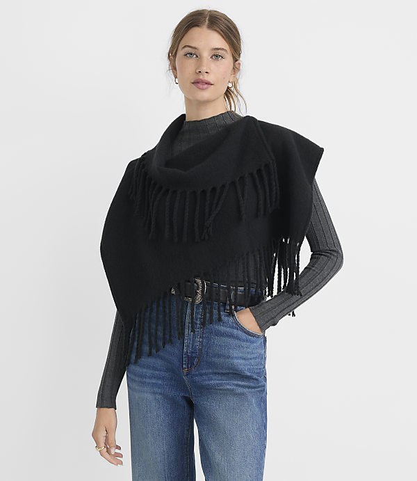 A woman in a black fringed shawl and jeans stands against a plain gray background.