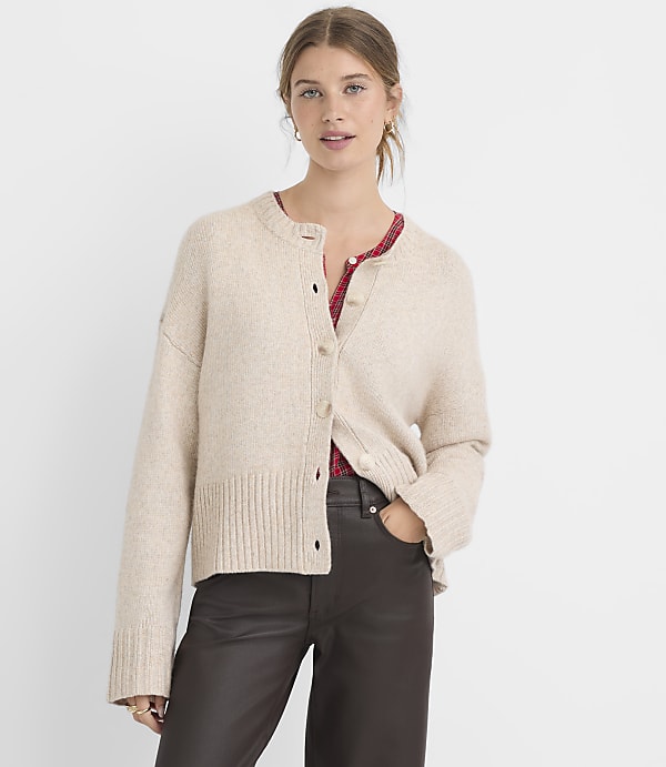 A woman in a beige cardigan and dark pants stands against a plain white background.