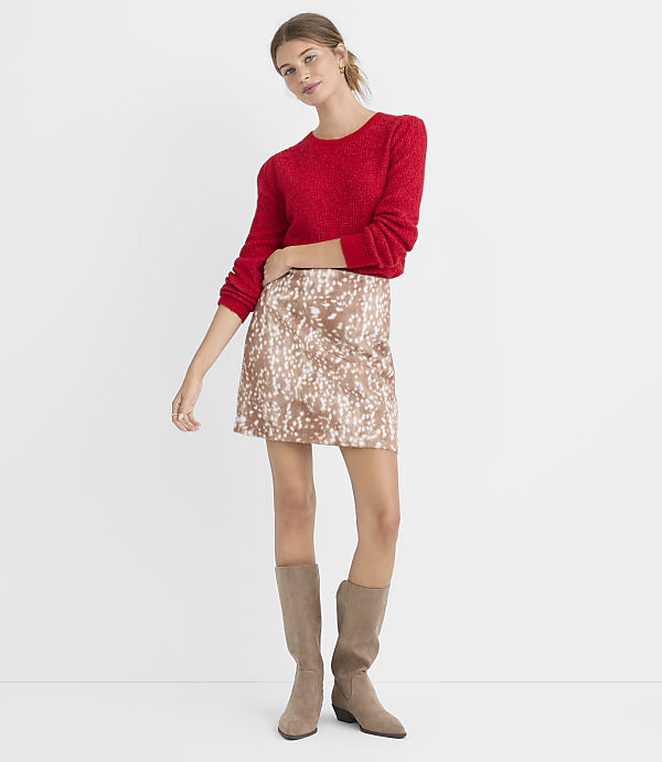 A woman in a red sweater and a patterned skirt stands against a plain white background.