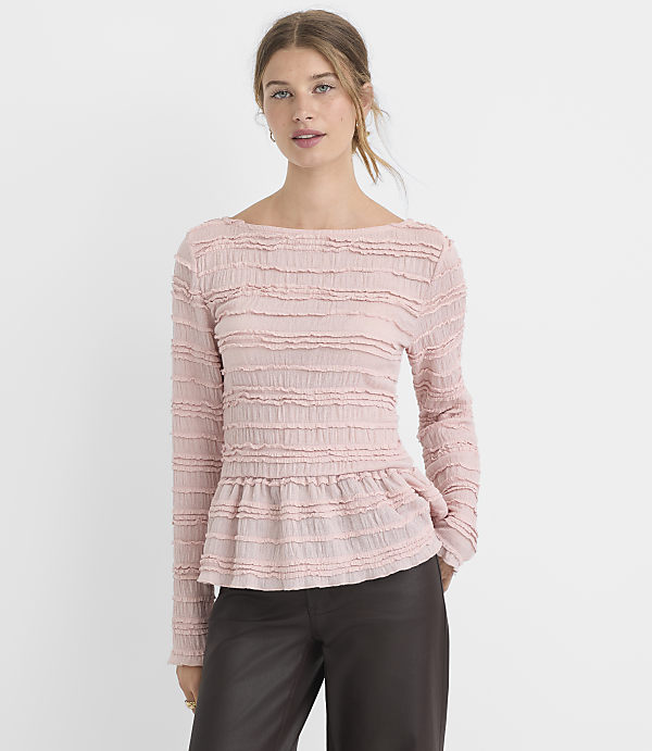 A woman in a pink textured peplum top and dark pants stands against a plain white background.