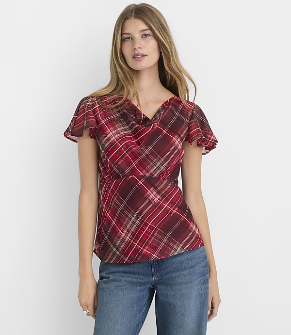 A woman in a red plaid blouse and blue jeans stands against a plain white background.
