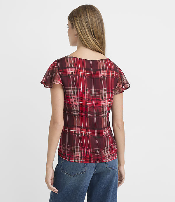 A woman in a red plaid top and blue jeans stands against a plain white background.