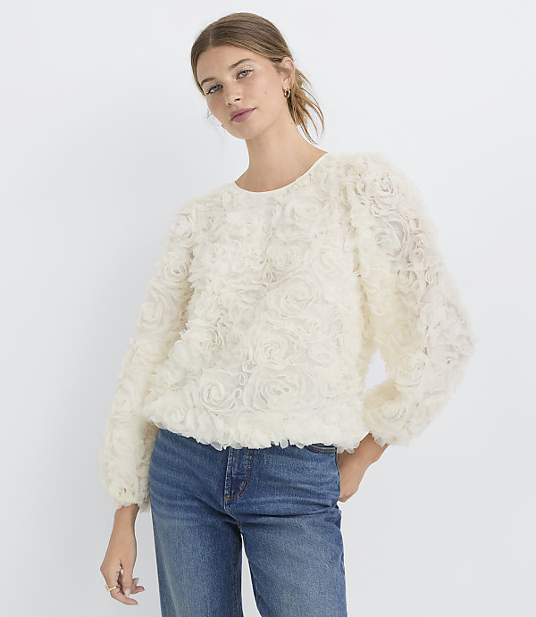 A woman in a textured cream blouse and blue jeans stands against a plain white background.
