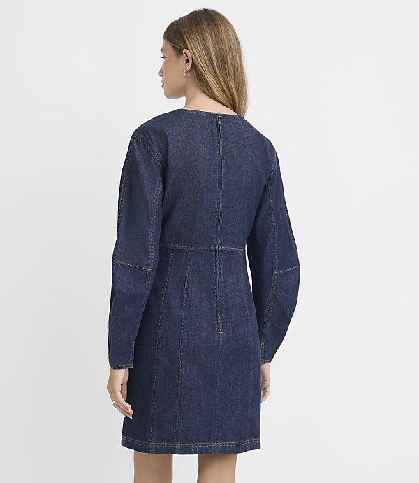 A woman in a dark denim dress stands against a plain white background.