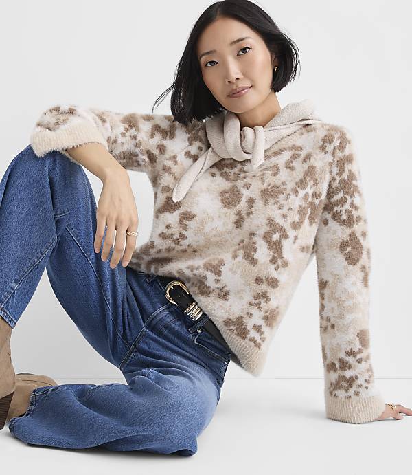 A woman wearing a leopard-print sweater and blue jeans sits against a plain white background.