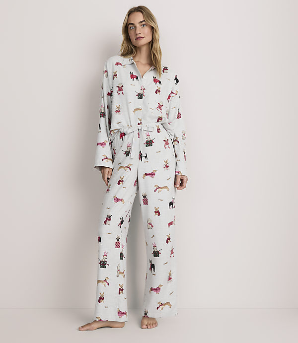 A woman stands wearing light blue dog-patterned pajamas against a plain, neutral background.