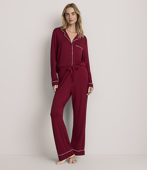 A woman wearing red pajamas with white trim stands against a plain, light-colored background.