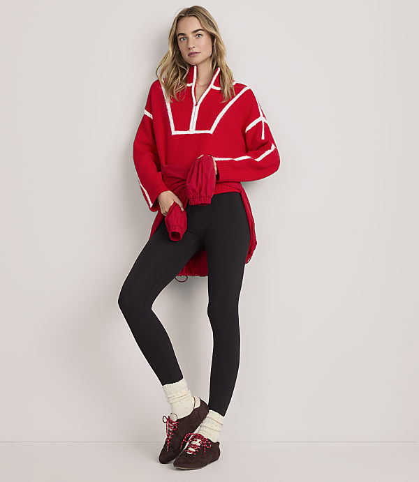 A woman wearing a red oversized sweater, black leggings, and brown boots stands against a plain white background.