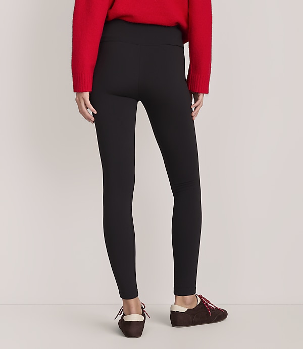 A person wearing a red sweater, black leggings, and brown shoes stands against a plain, light-colored background.