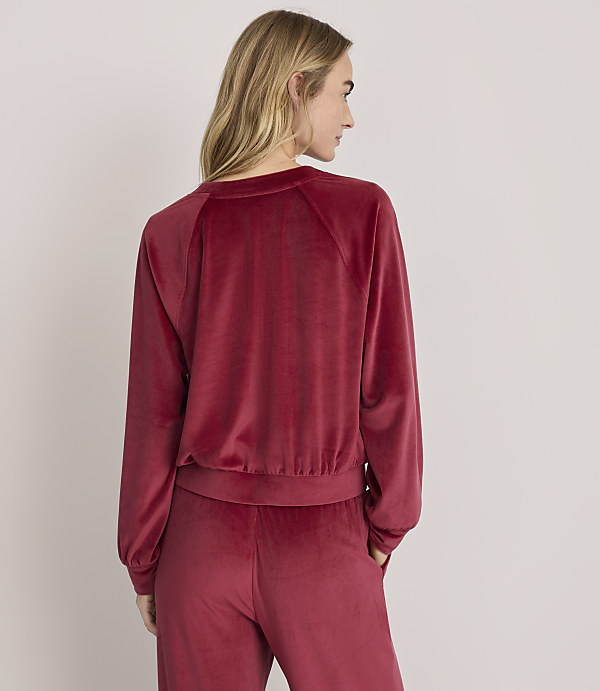 A woman wearing a red velvet tracksuit stands with her back to the viewer against a plain white background.