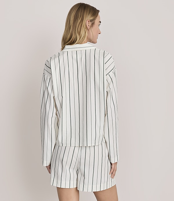 A woman stands with her back to the camera wearing a white and green striped matching shirt and shorts set against a plain light grey background.