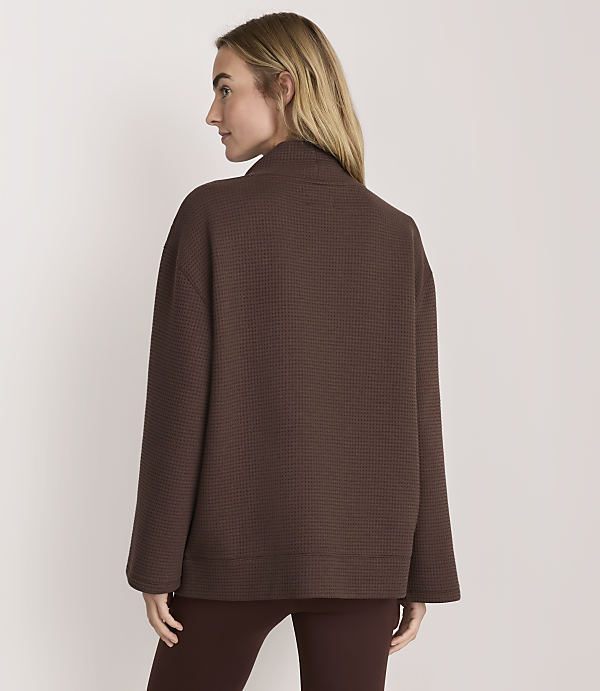 A woman wearing a brown textured jacket and matching leggings stands against a plain white background.