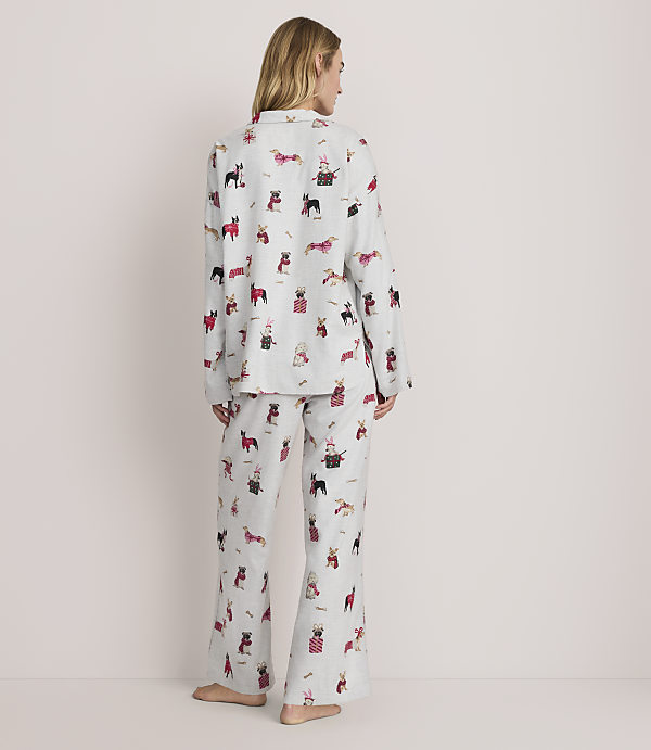 A woman stands with her back to the camera wearing light grey pajamas with a dog print against a plain, light-colored background.