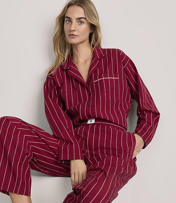 A blonde woman wearing red and white striped pajamas poses against a plain white background.