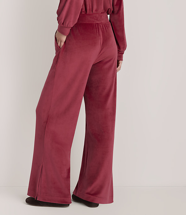 A person wears wide-leg red velvet trousers and a matching top against a plain, light-colored background.